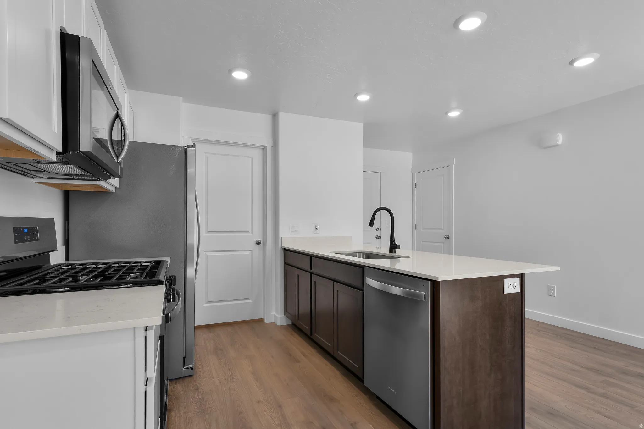 Kitchen featuring an island with a sink, white countertops, dark wood-finish cabinetry, stainless steel appliances, and recessed lighting