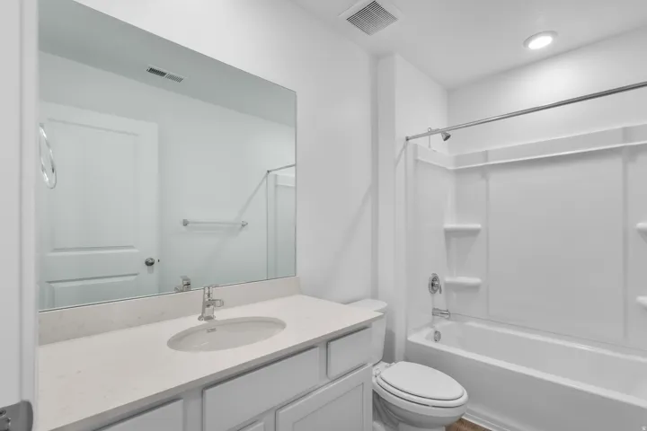 Bathroom featuring a white vanity with an undermount sink, a light-toned countertop, a large wall mirror, and a white bathtub with an integrated shower