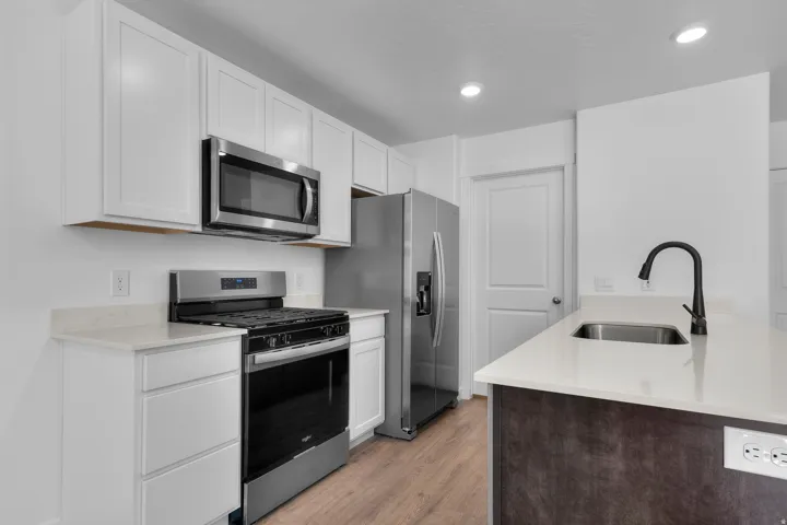 Kitchen featuring white shaker cabinetry, stainless steel appliances, light-toned countertops, a stainless steel sink, and wood-finish flooring
