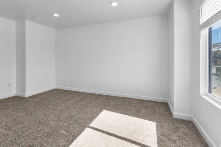 Recessed ceiling lighting, neutral tone carpet, white wall finishes, and a single window with blinds