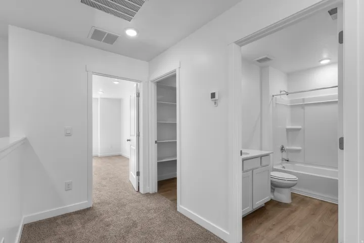 Carpeted hallway with recessed lighting, an interior room with carpeting, a built-in linen closet with shelving, and a bathroom featuring a shower-tub combination, vanity, and wood-finish flooring