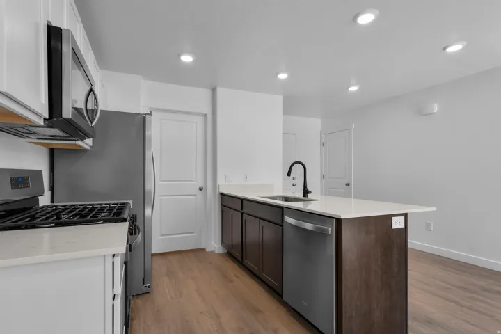Kitchen featuring an island with a sink, white countertops, dark wood-finish cabinetry, stainless steel appliances, and recessed lighting
