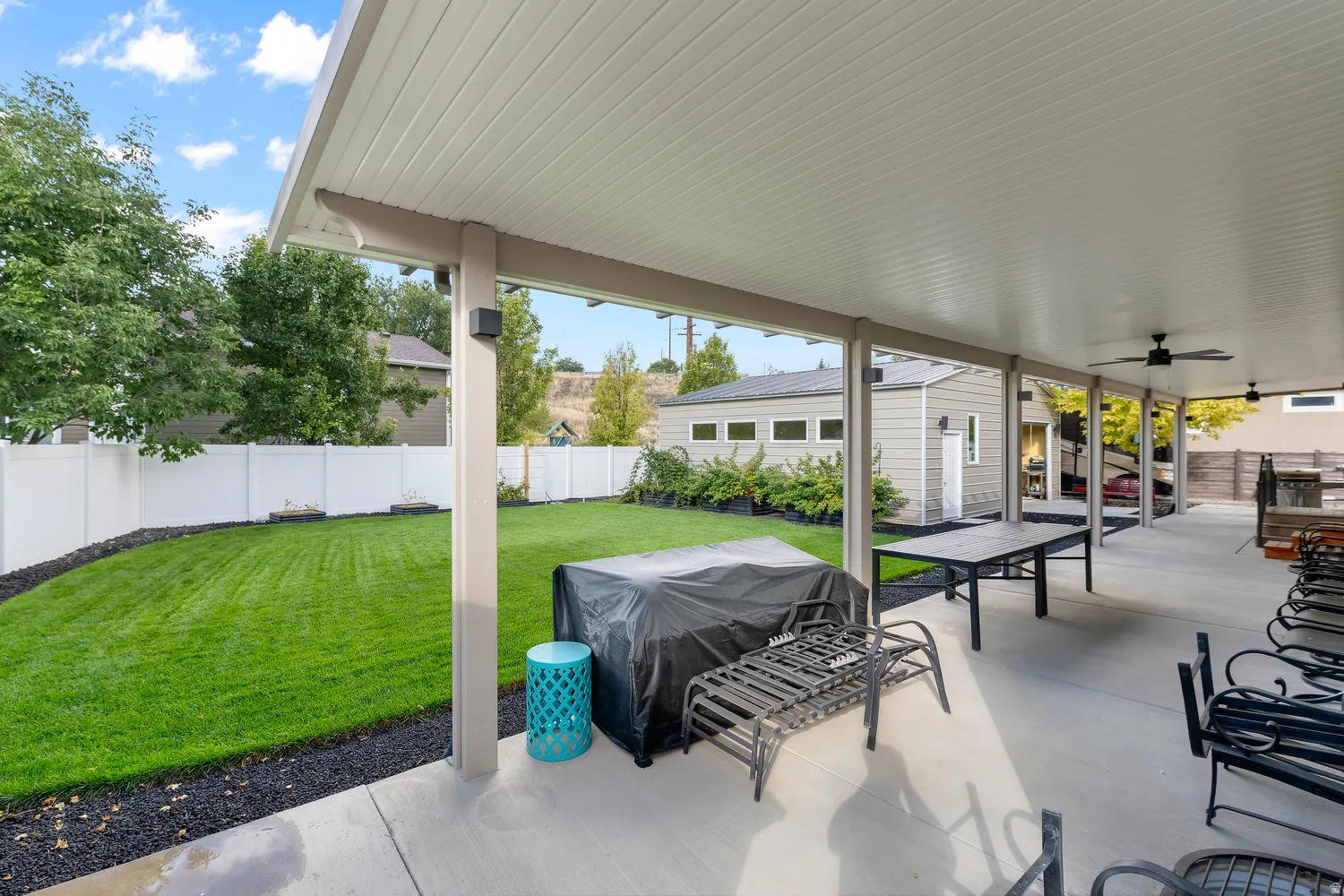 Expansive covered patio with multiple ceiling fans, overlooking a manicured lawn and privacy fencing