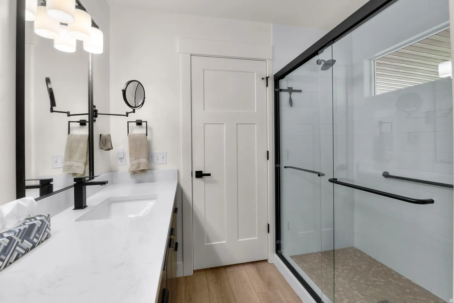 Huge walk in master shower, Modern bathroom featuring a glass-enclosed shower with subway tile, wood-finish flooring, a contemporary vanity with a white countertop, and matte black fixtures