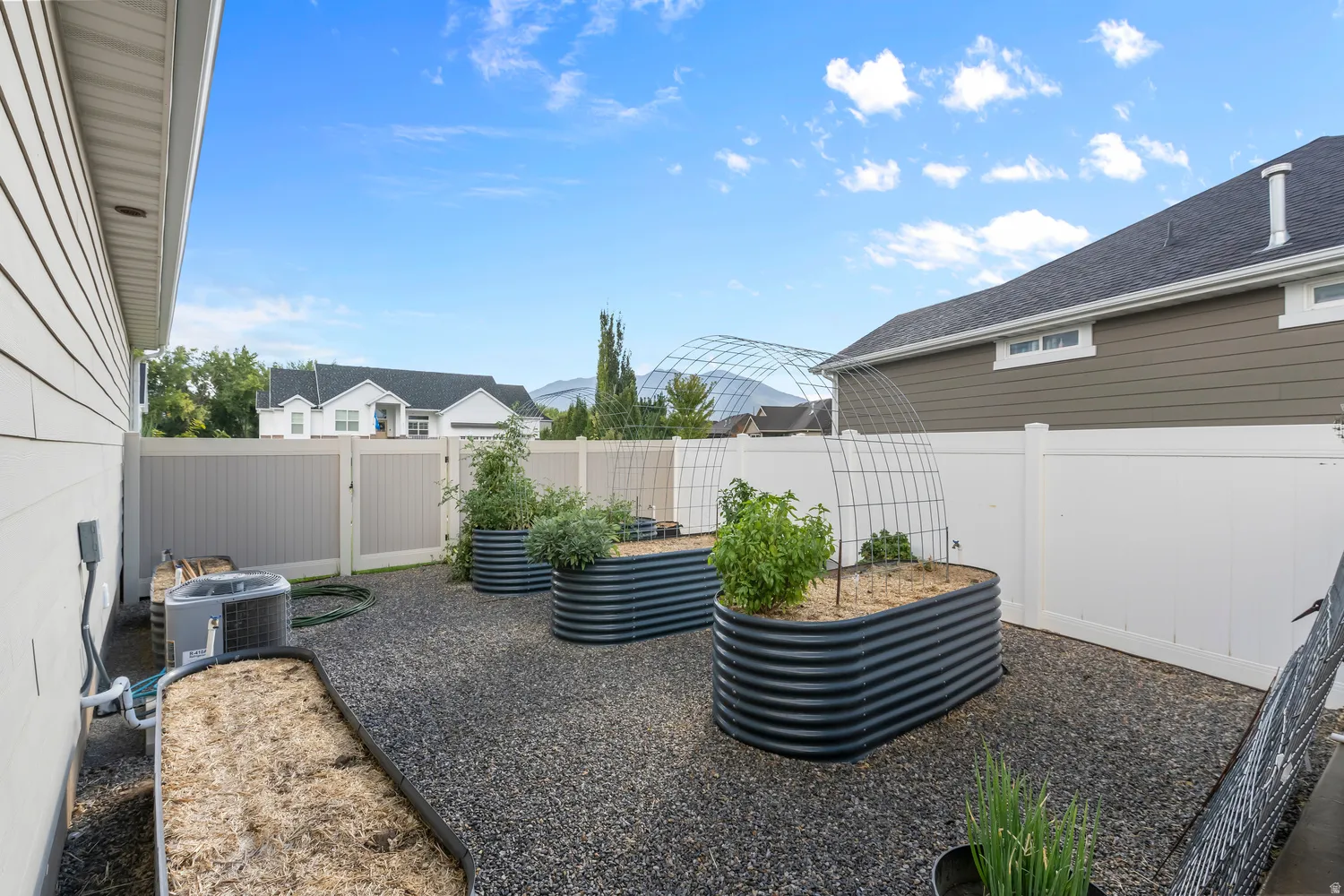 Landscaped backyard featuring multiple raised garden beds, gravel ground cover, and full perimeter fencing