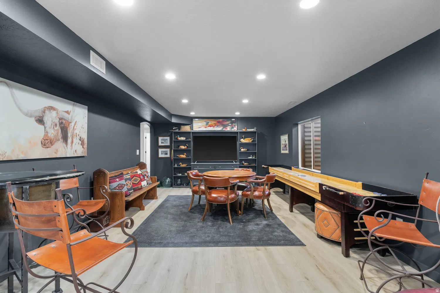 Recessed lighting, light wood-finish flooring, built-in shelving, dark-painted walls, and a window with horizontal blinds