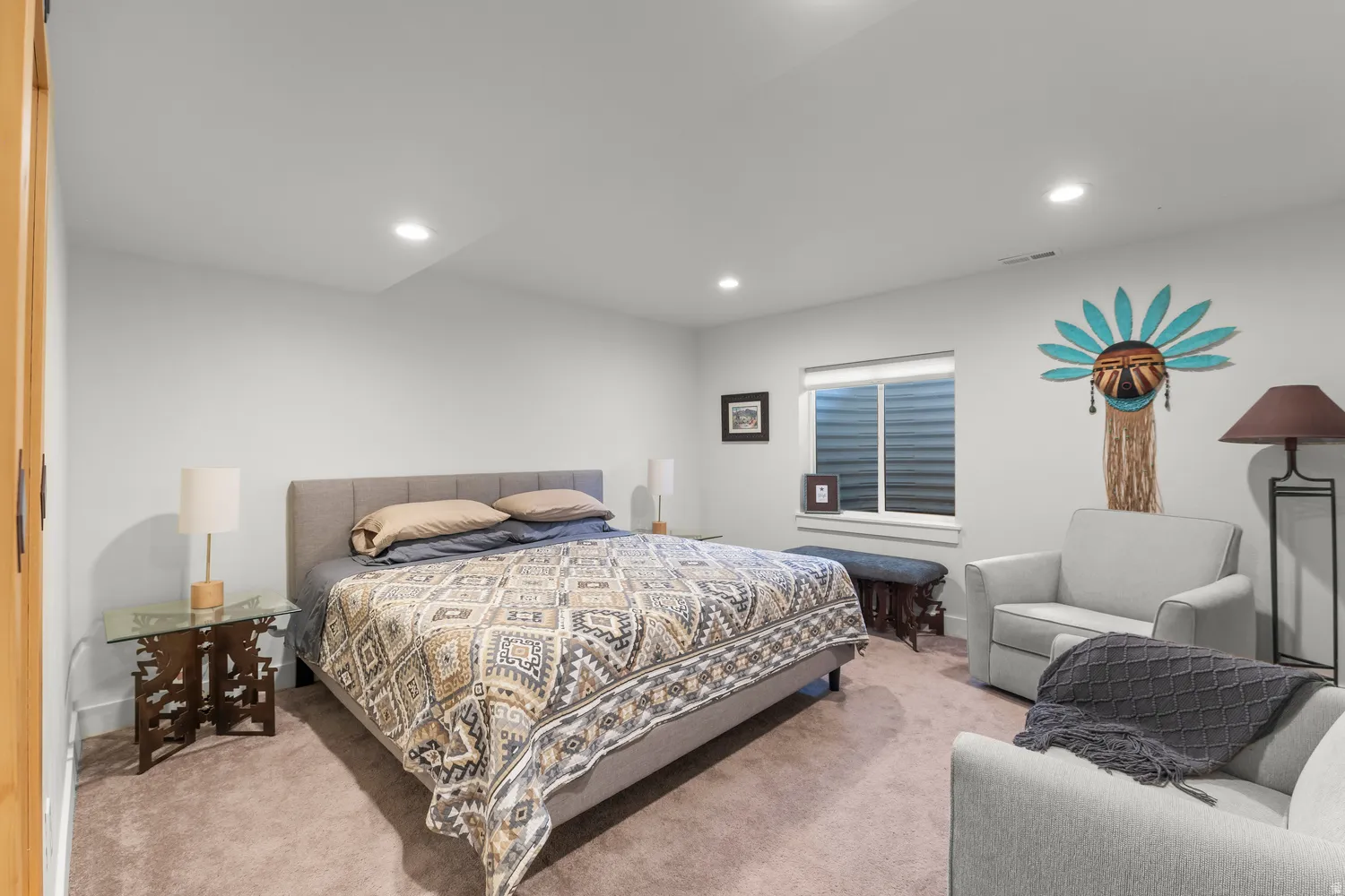Recessed lighting, wood-finish door, light-colored wall paint, carpet flooring, and a large window with blinds