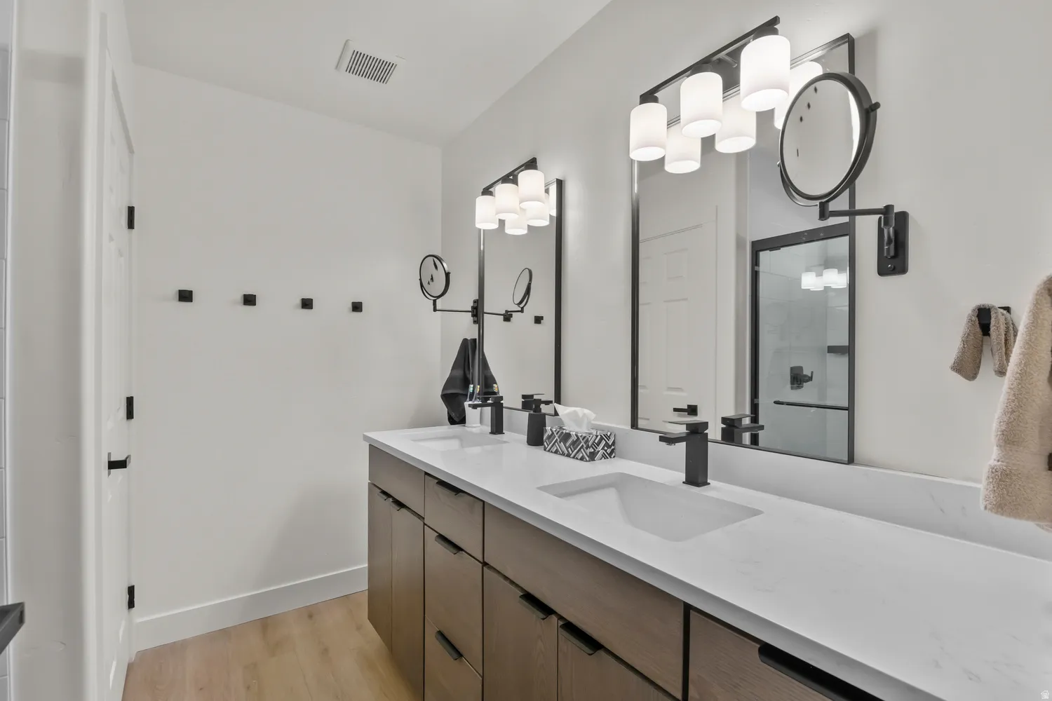 Master bath, Dual vanity with wood-finish cabinetry, white stone countertops, and matte black fixtures