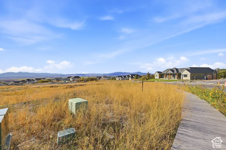Wide open land with a curved wood-finish pathway and distant homes under a clear sky