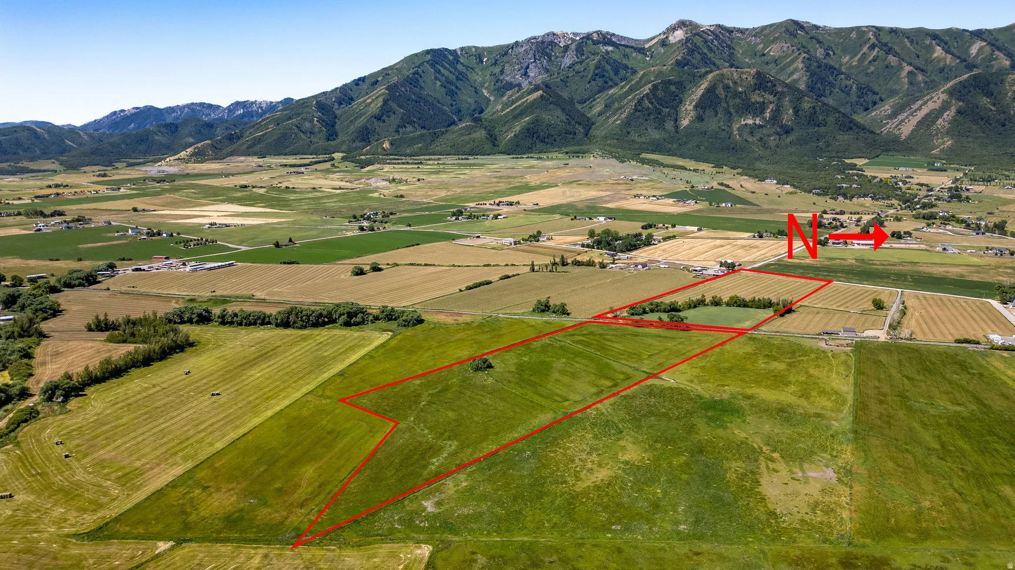 Expansive green fields with delineated property lines, surrounded by a rural landscape and distant mountains