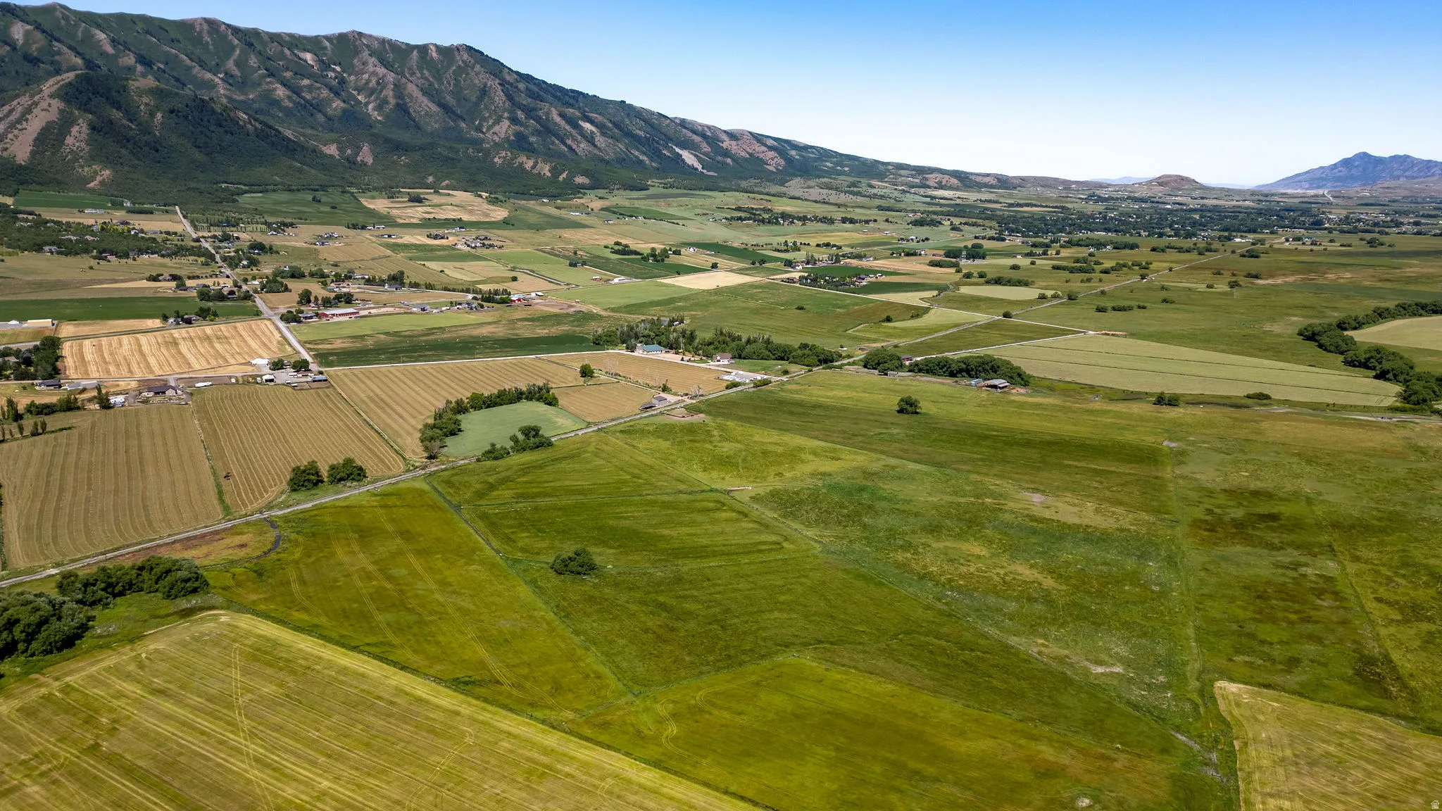 Expansive green and cultivated fields with distant mountainous terrain and scattered buildings
