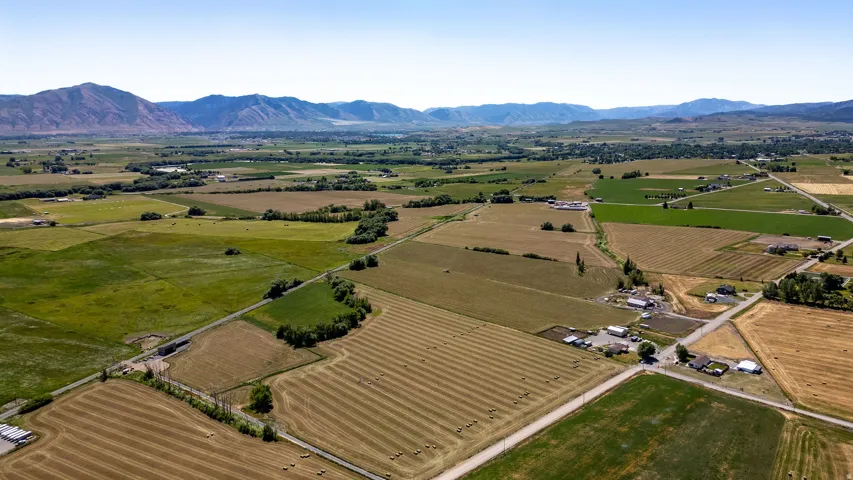 Expansive agricultural landscape with diverse fields, distant mountain range, scattered residential structures, and established road infrastructure