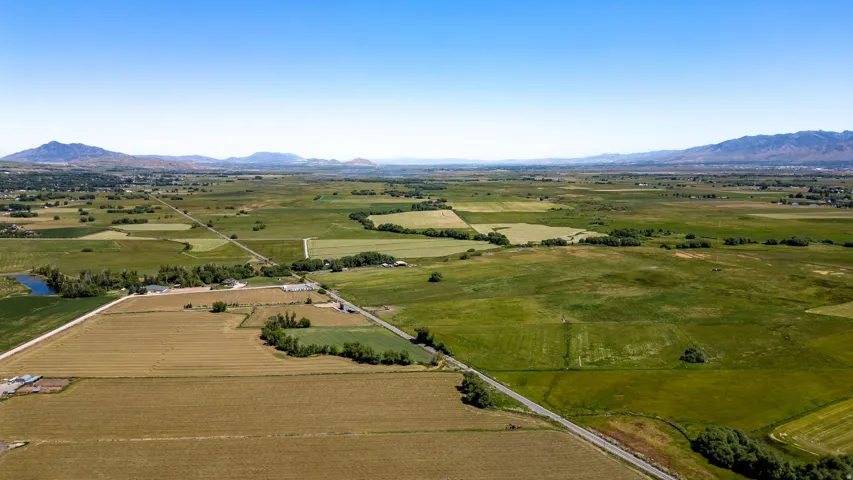 Expansive property featuring a clear blue sky, distant mountains, varied agricultural fields, and established roadways