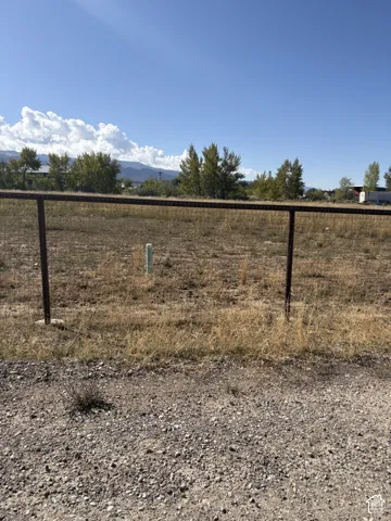 Expansive lot featuring a wire fence, natural ground cover, and a clear blue sky