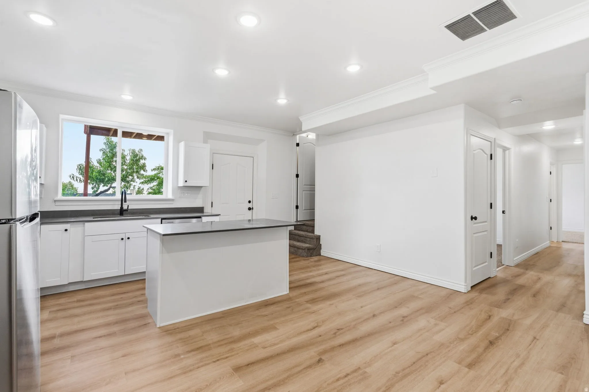 Bright kitchen featuring white cabinetry, dark countertops, a central island, and wood-finish flooring