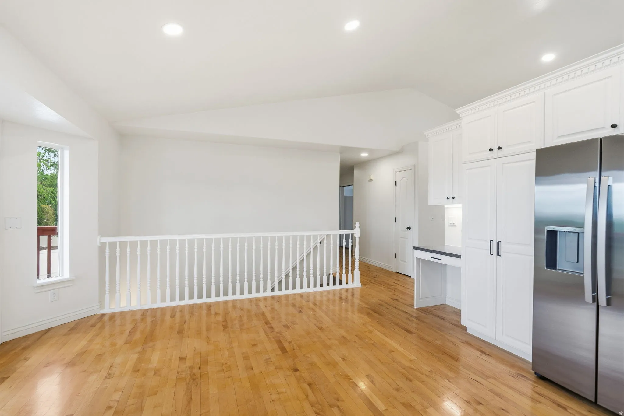Hardwood flooring throughout, recessed lighting, white wood cabinetry with black hardware, stainless steel refrigerator, and built-in desk area