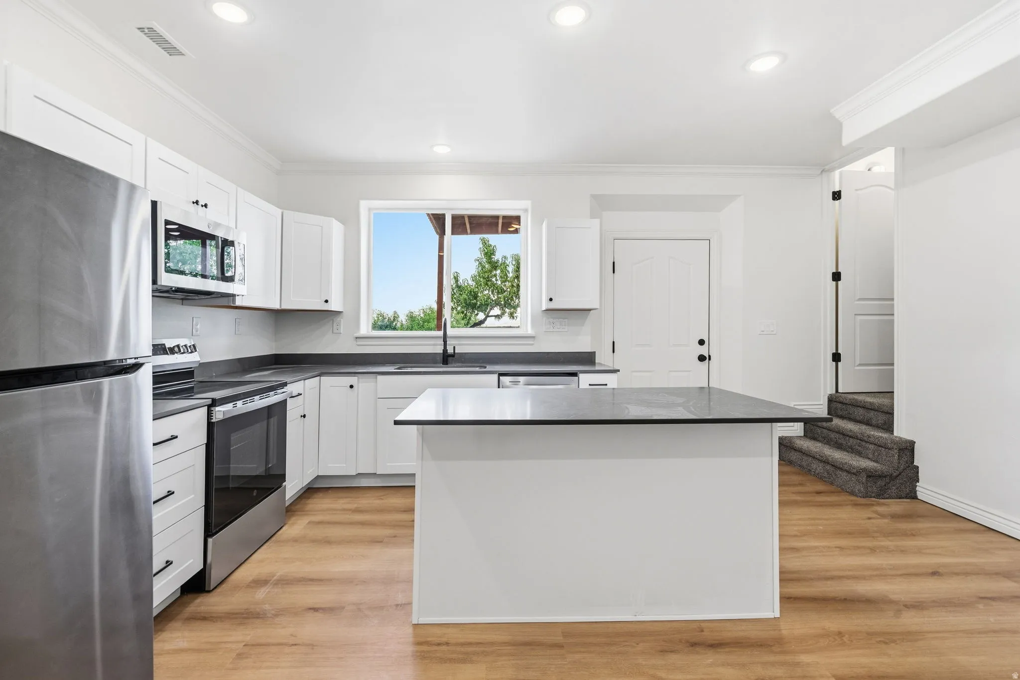 Kitchen featuring white shaker cabinetry, stainless steel appliances, dark countertops, a central island, and wood-finish flooring