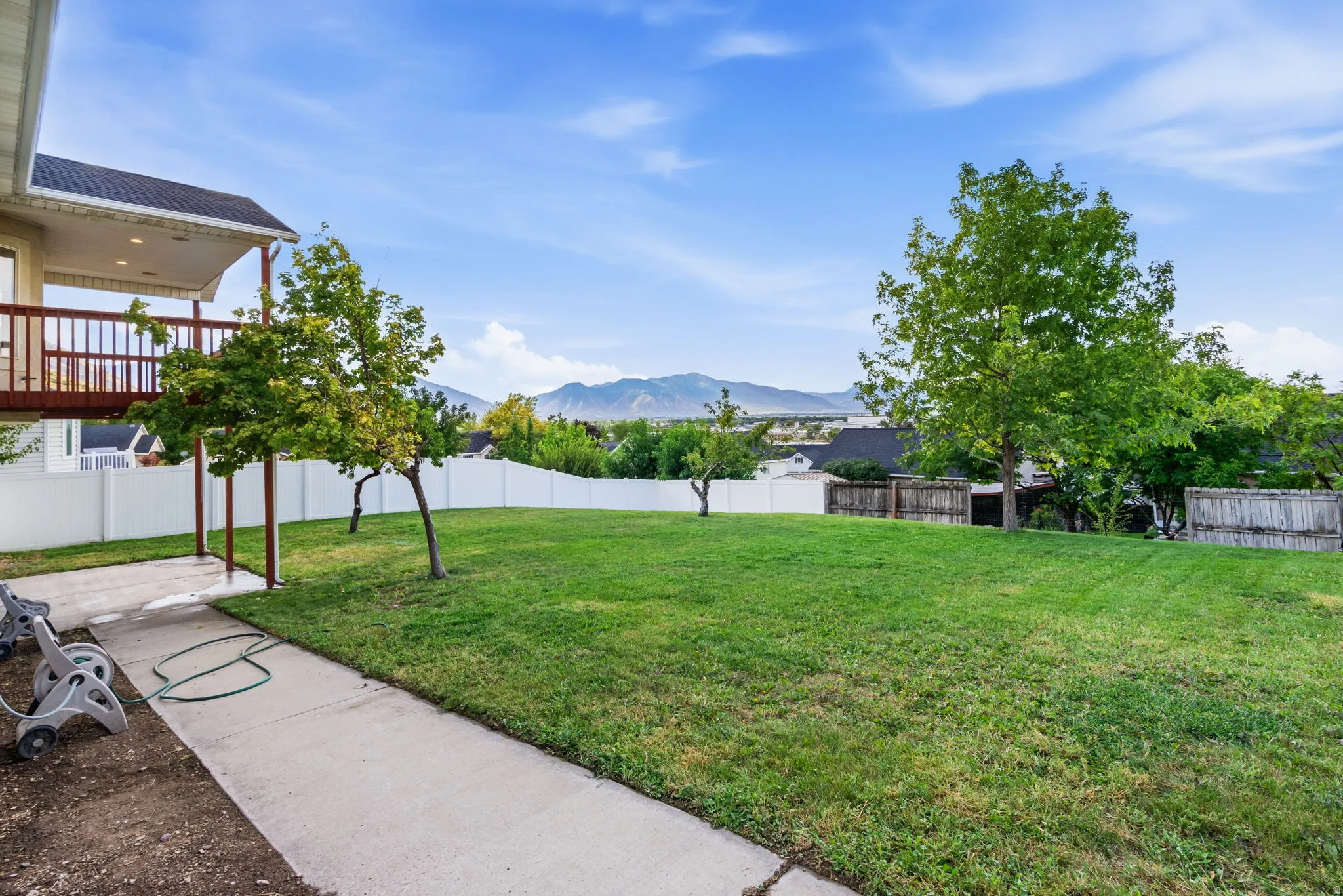 Expansive backyard with a lush lawn, mature trees, concrete patio, and a privacy fence