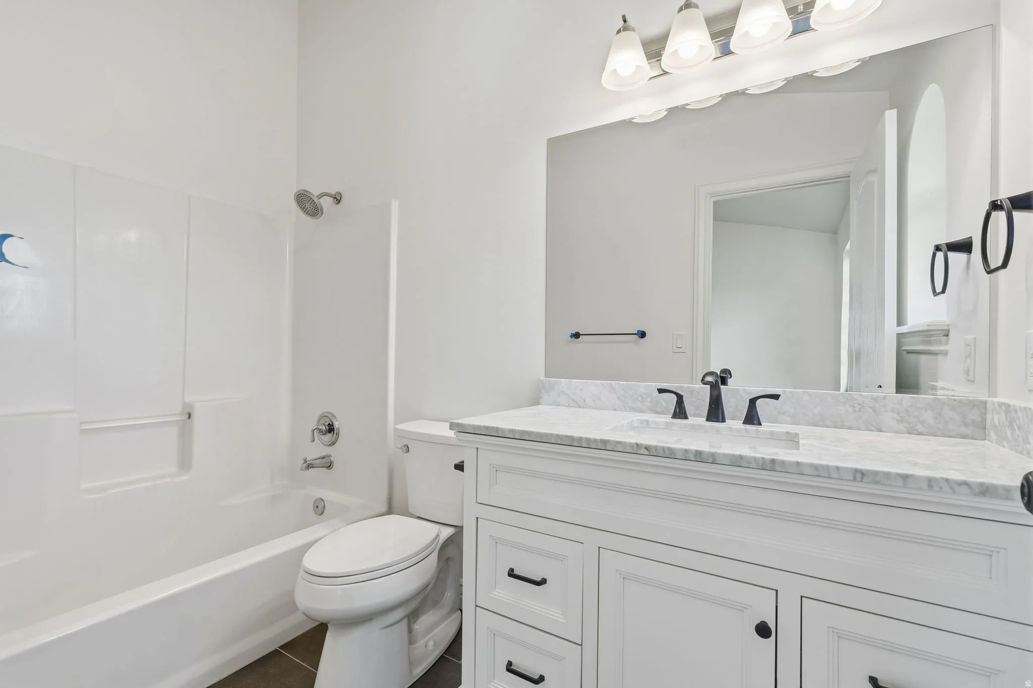 White vanity with cabinet storage, stone countertop, matte black fixtures, and a shower/tub combination