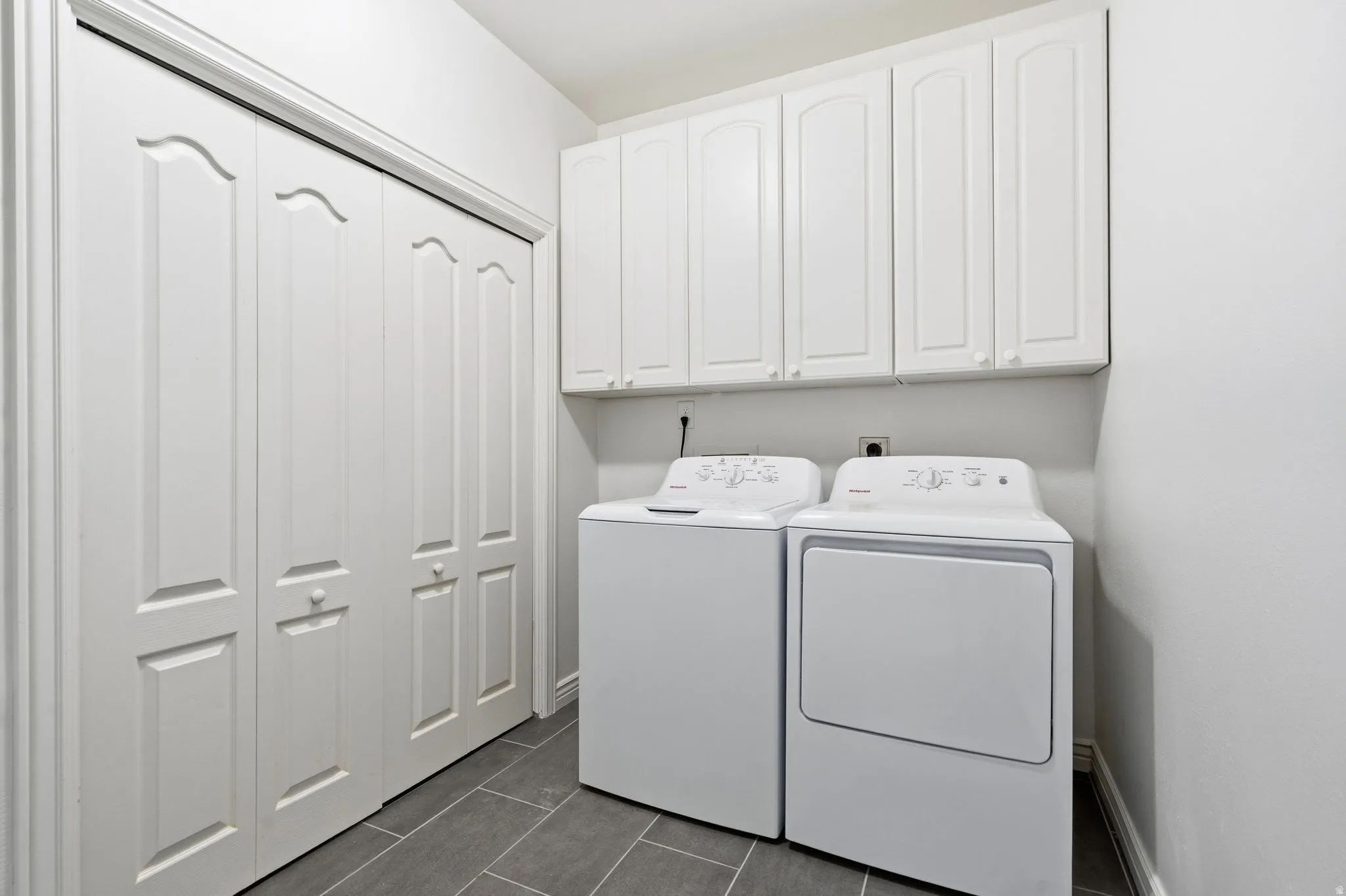 White bi-fold closet doors, white upper cabinetry, and gray tile flooring
