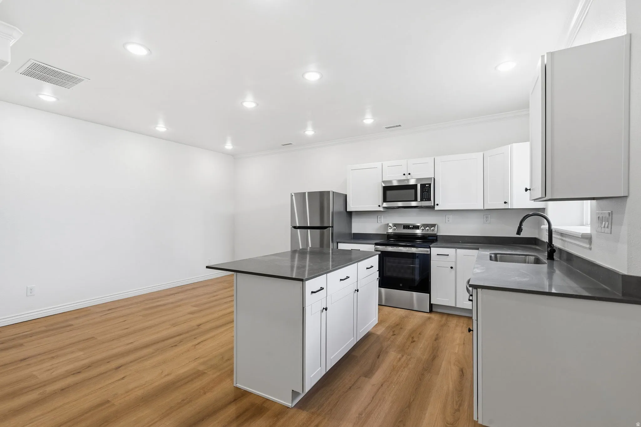 Modern kitchen featuring stainless steel appliances, white cabinetry, dark countertops, a central island, and wood-finish flooring