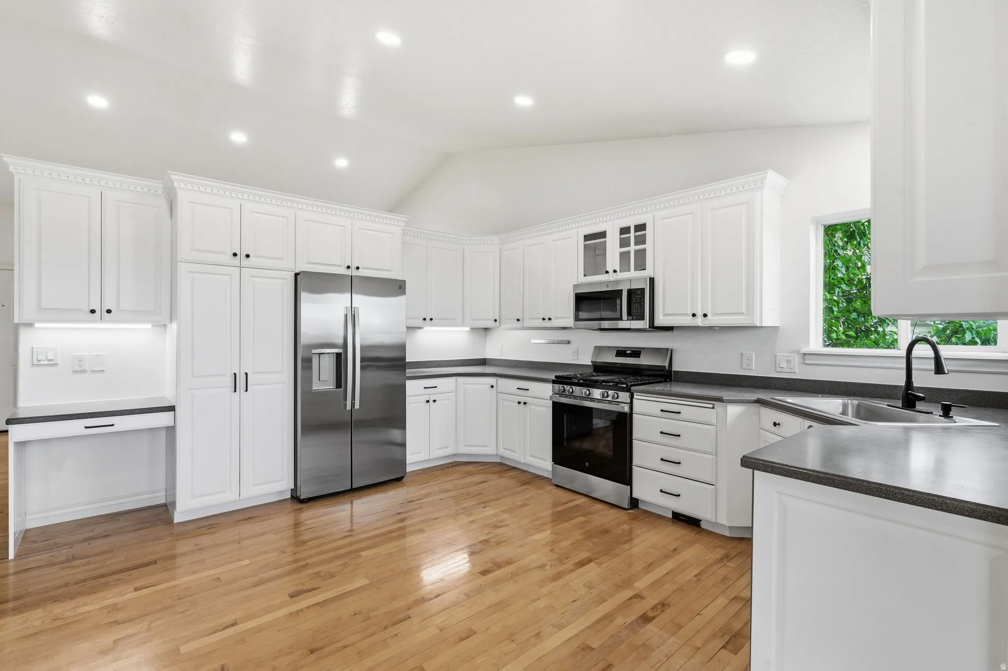 Kitchen featuring white cabinetry, stainless steel appliances, wood-finish flooring, recessed lighting, and a built-in desk