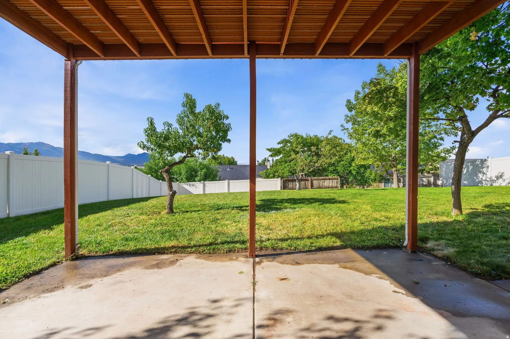 Covered patio area with a slatted wood ceiling, concrete flooring, and an expansive lawn