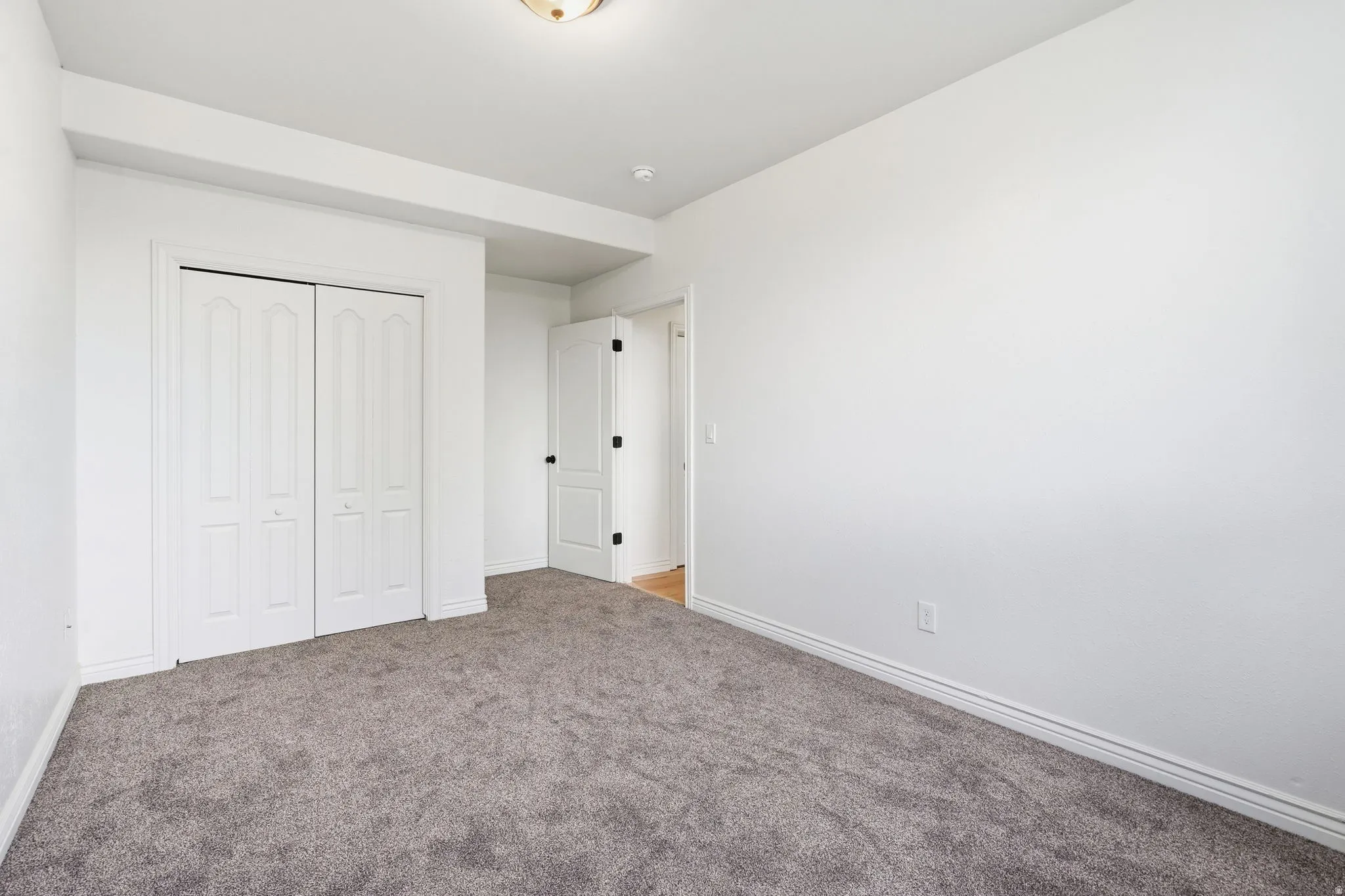 Neutral gray carpeting, white walls, white bi-fold closet doors, white baseboards, and a semi-flush mount ceiling light
