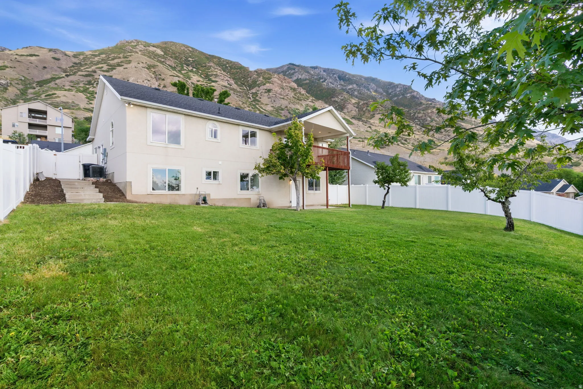 Expansive backyard with a manicured lawn, established trees, and white privacy fencing