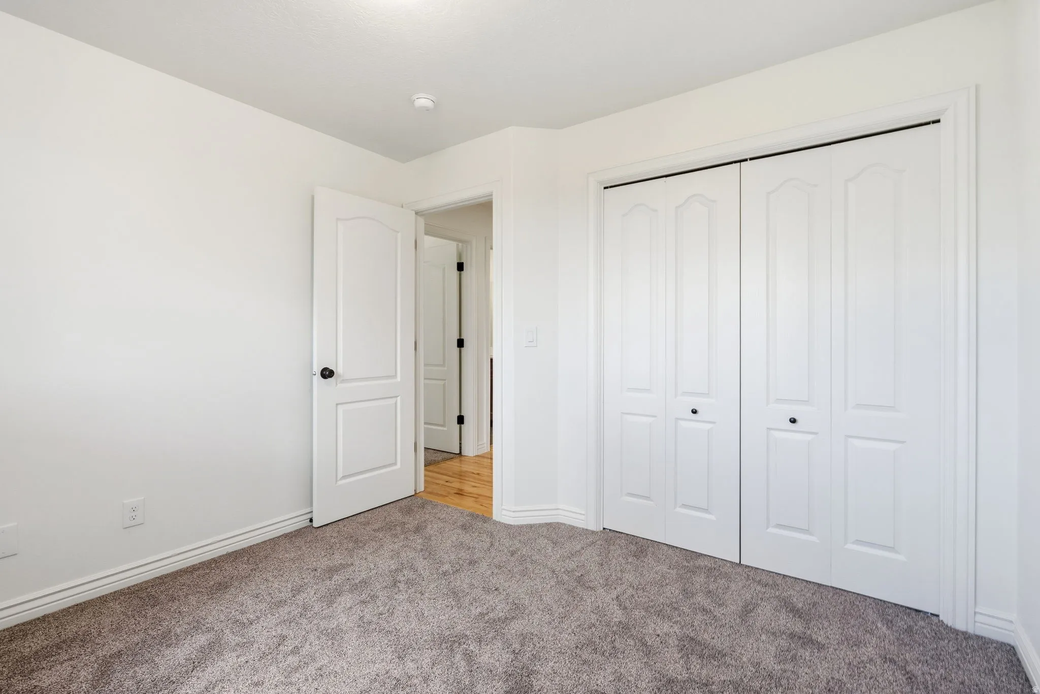 Plush gray carpeting, white trim, white paneled doors, and a built-in closet with bi-fold doors