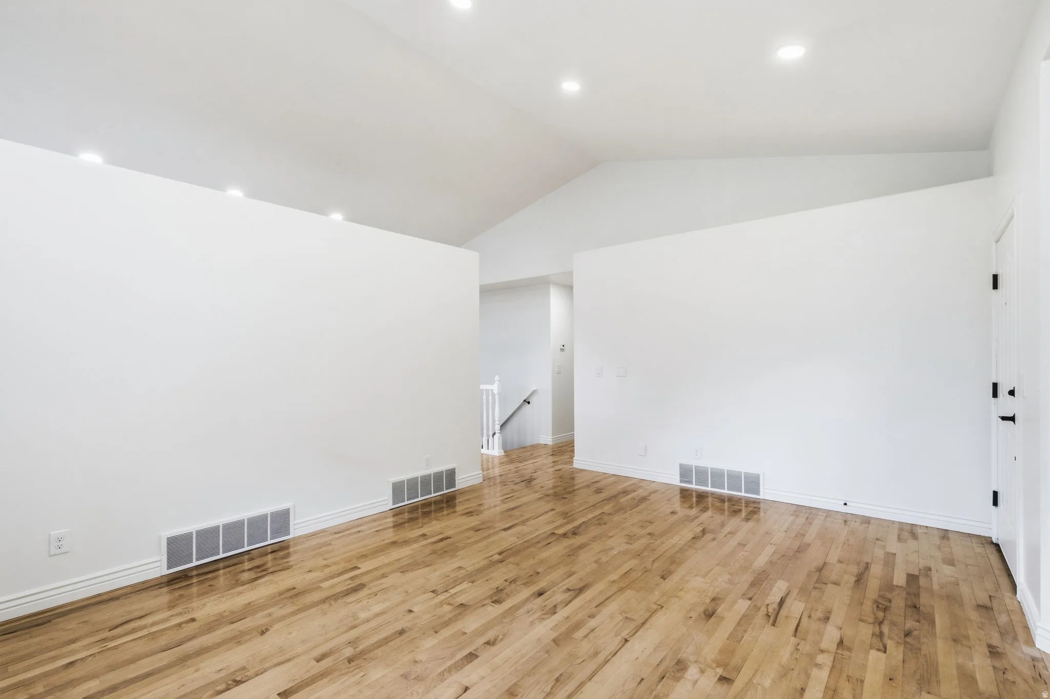 Vaulted ceiling with recessed lighting, light wood-finish flooring, and white interior walls