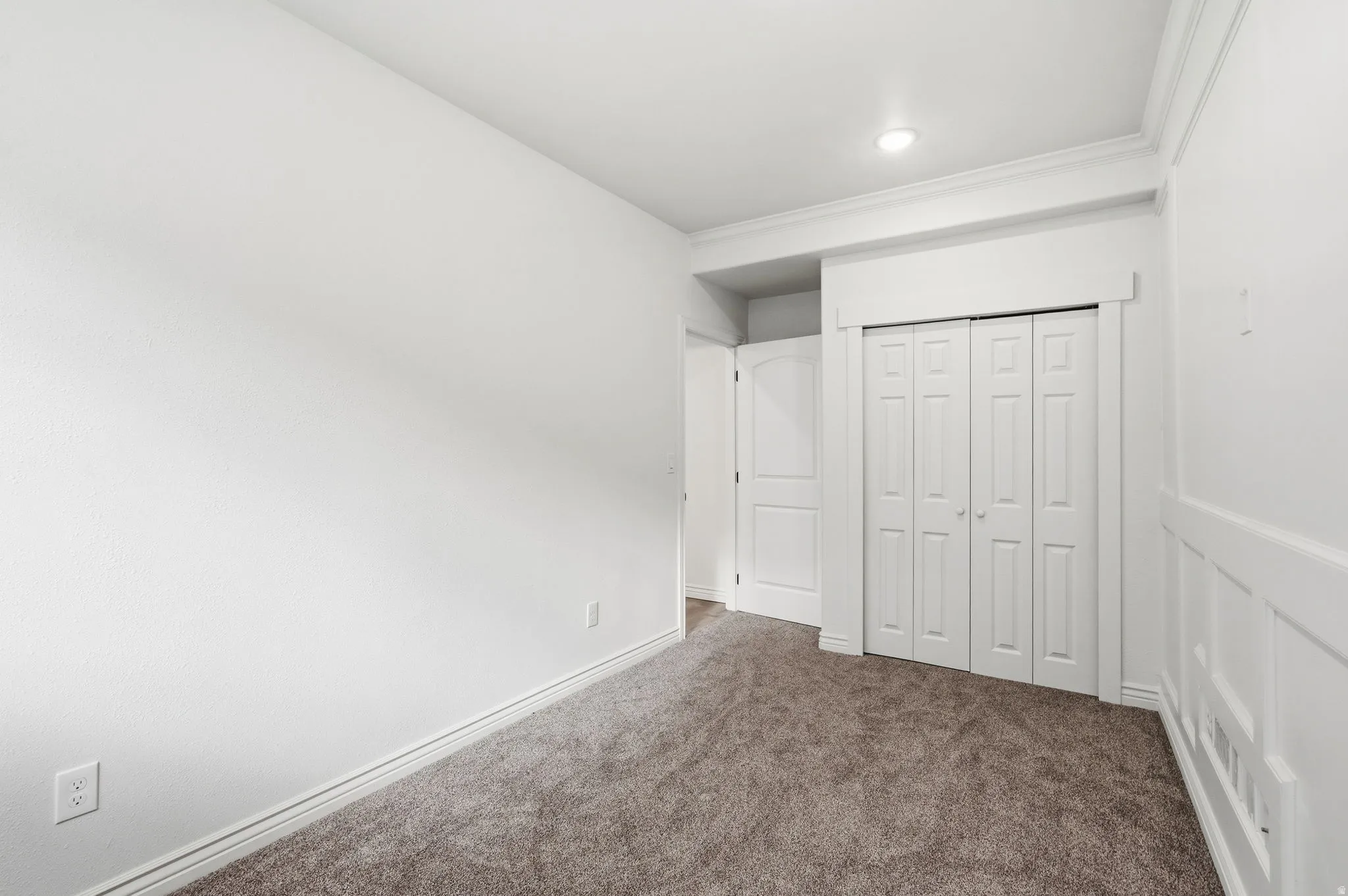Recessed lighting, crown molding, paneled accent wall, bi-fold closet doors, and neutral carpeting