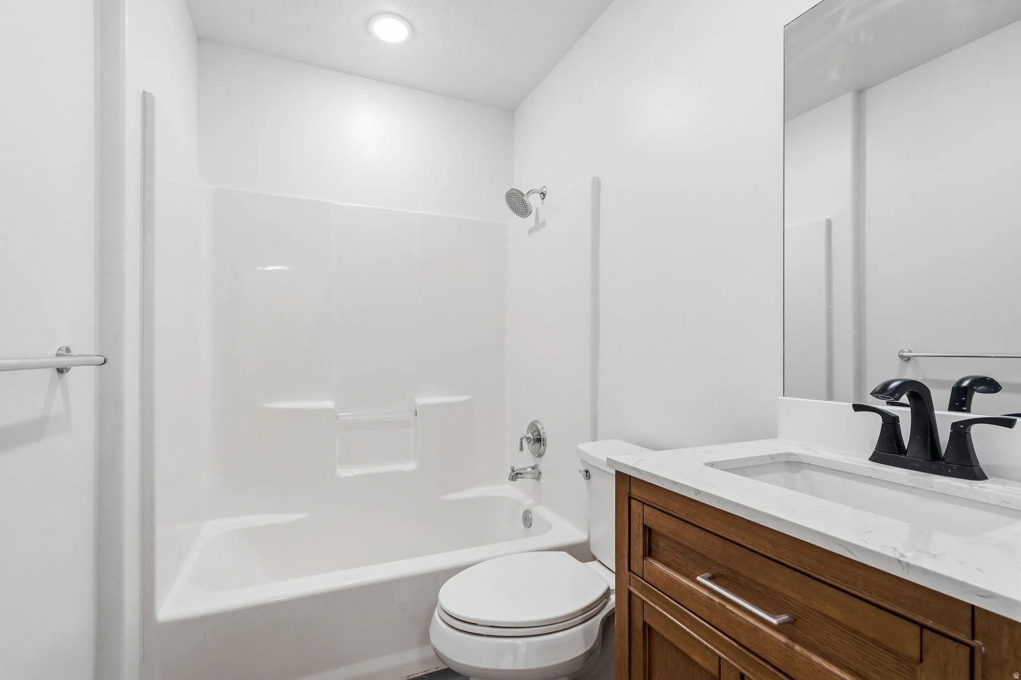White tub and shower combination with a single-handle faucet, wood-finish vanity with a white countertop, and a rectangular sink with a matte black faucet