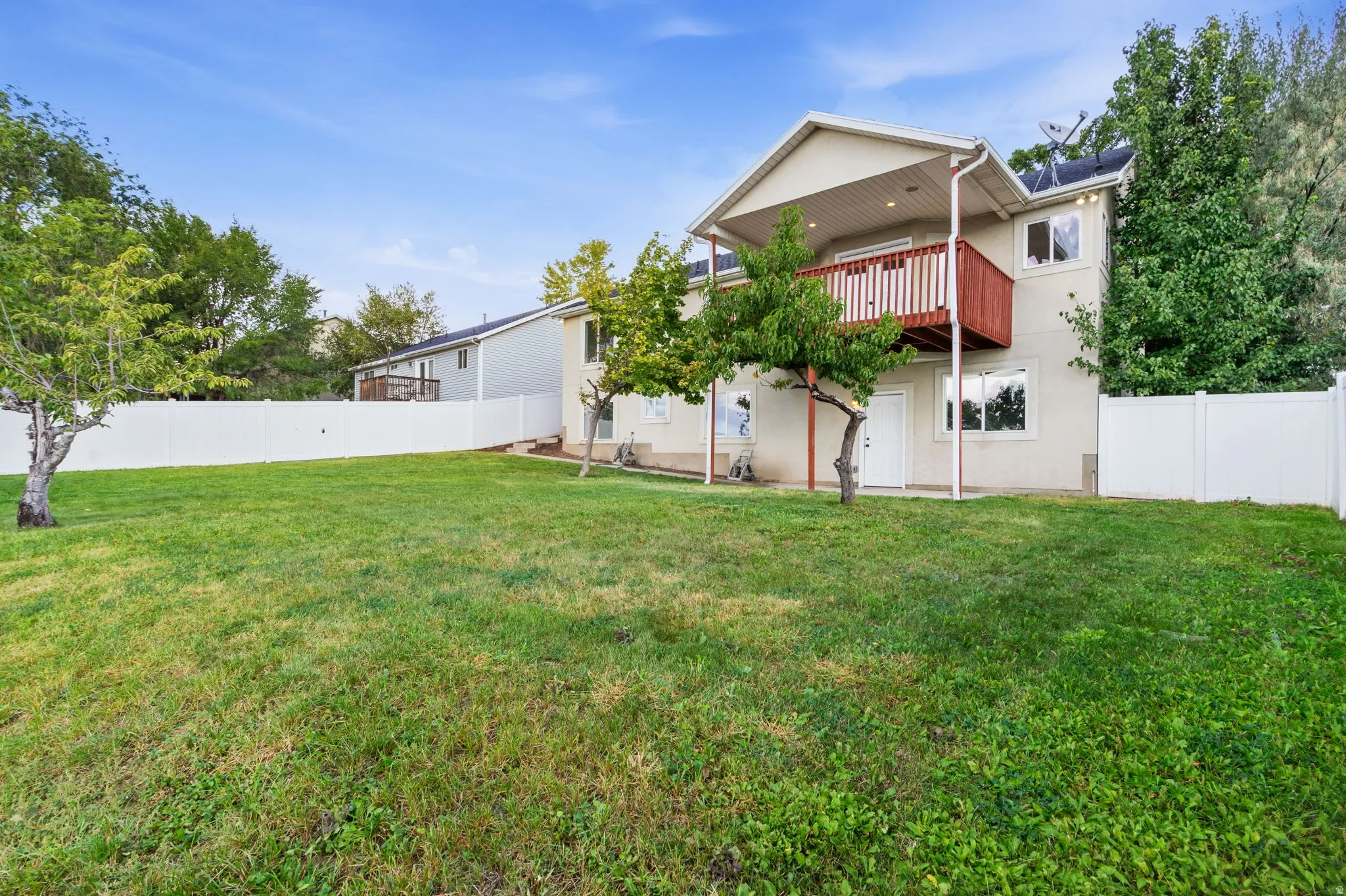 Expansive rear yard featuring a white vinyl fence, mature trees, and a two-story exterior with a second-level balcony