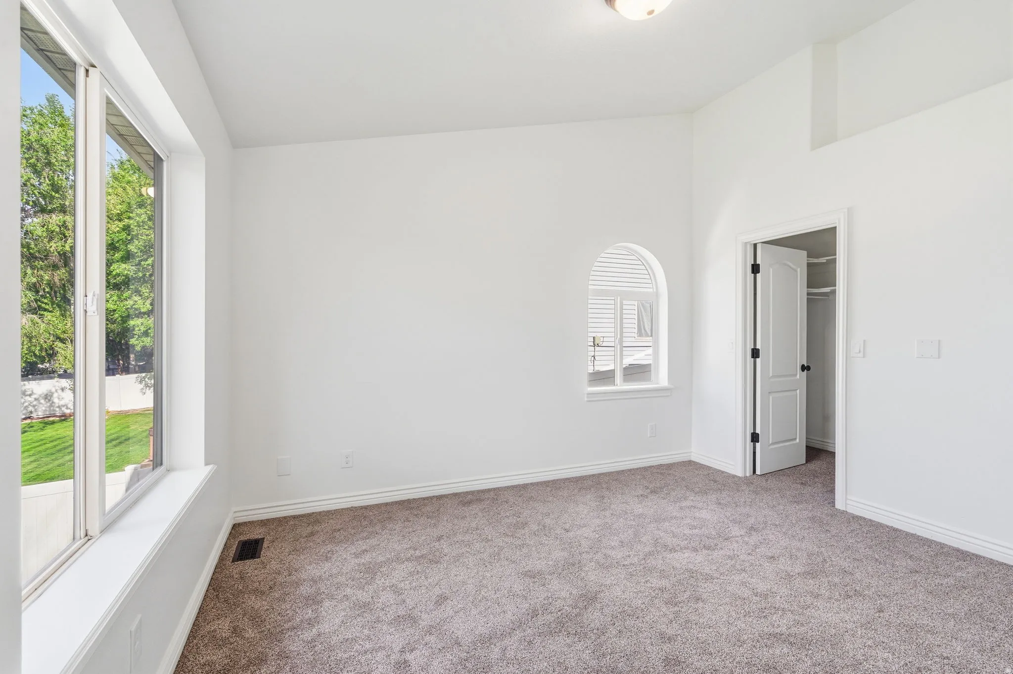 Spacious room featuring neutral carpeting, a large picture window, an arched window, and a white interior door
