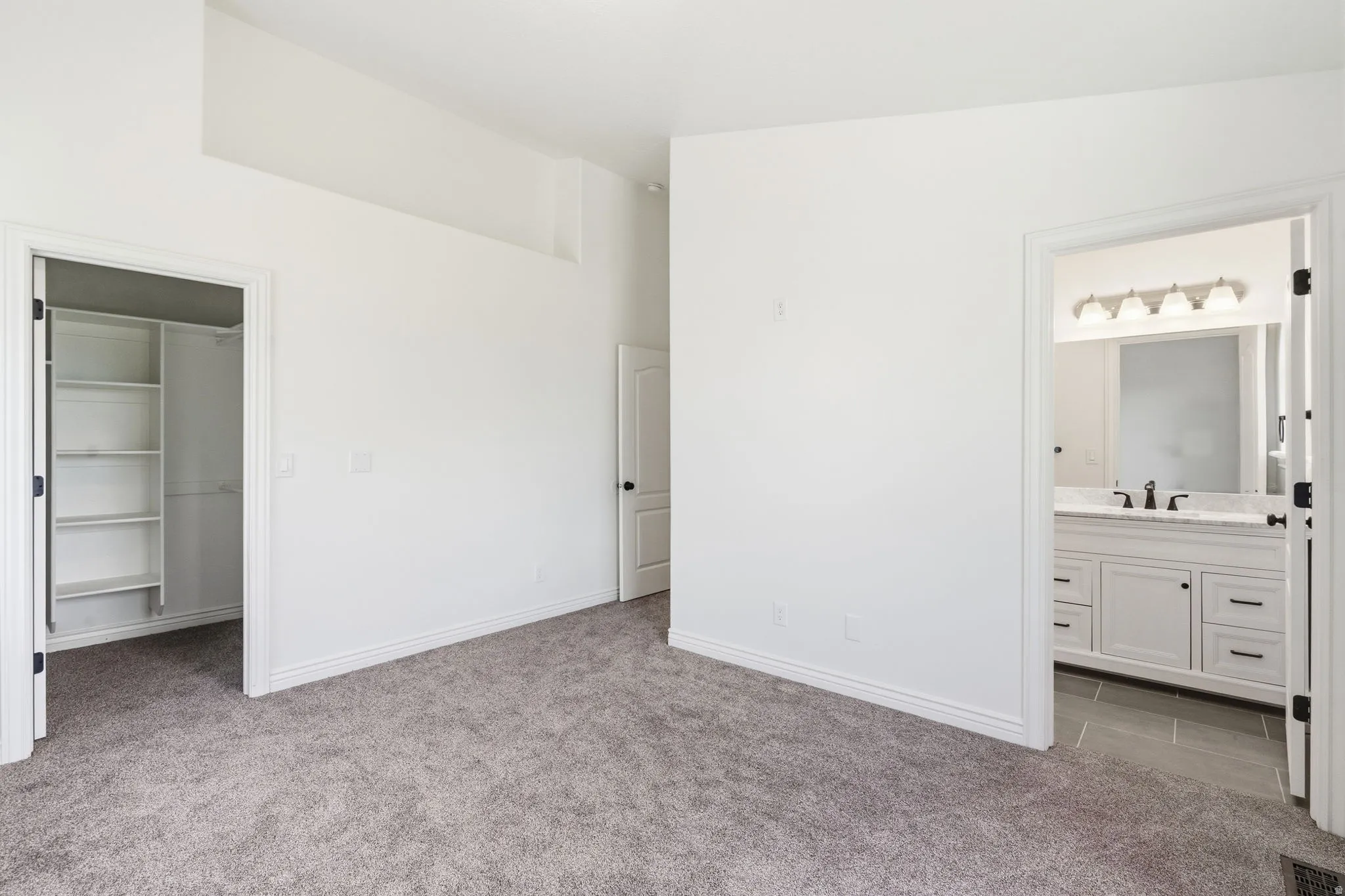 Vaulted ceiling, carpeted flooring, built-in closet shelving, white vanity with stone countertop, and tile flooring in bathroom