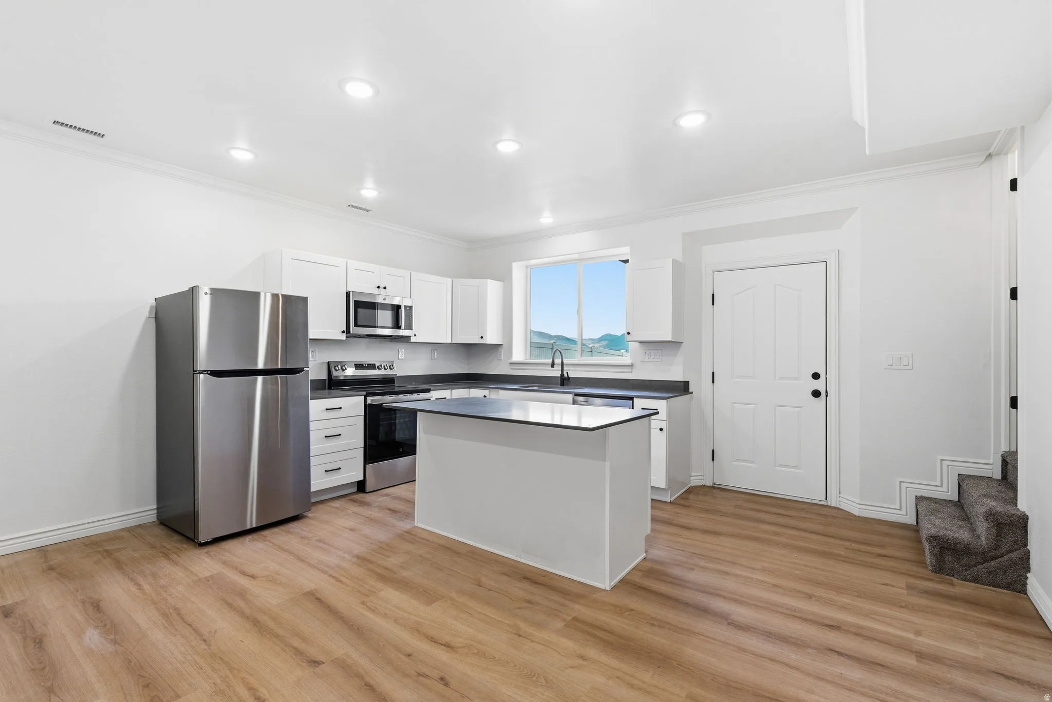 Kitchen featuring wood-finish flooring, white cabinetry, dark countertops, and stainless steel appliances