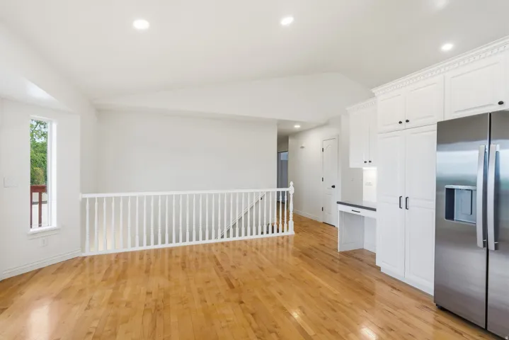 Hardwood flooring throughout, recessed lighting, white wood cabinetry with black hardware, stainless steel refrigerator, and built-in desk area