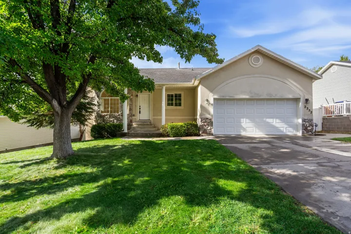 Stucco exterior with stone accents, a prominent two-car garage, mature front yard tree, and an inviting front entrance with covered porch