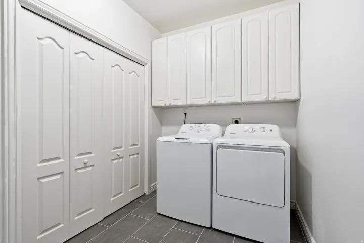 White bi-fold closet doors, white upper cabinetry, and gray tile flooring