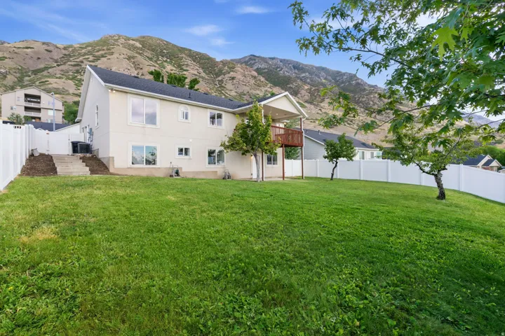 Expansive backyard with a manicured lawn, established trees, and white privacy fencing