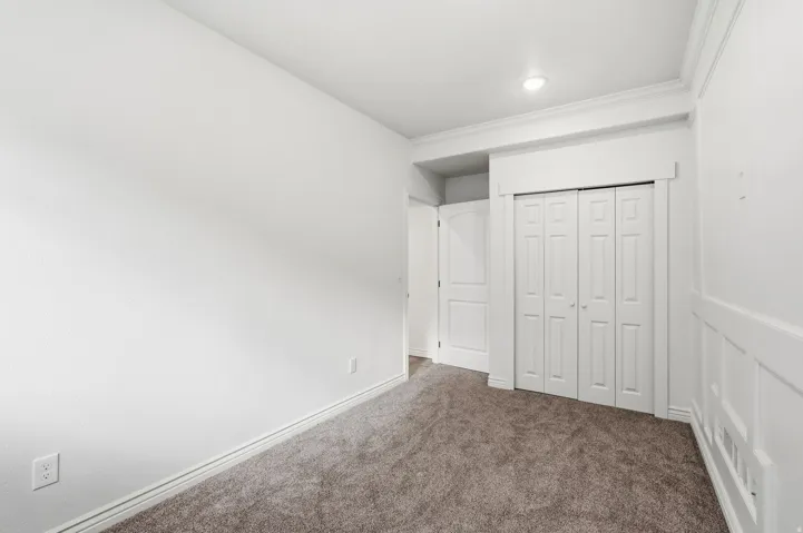 Recessed lighting, crown molding, paneled accent wall, bi-fold closet doors, and neutral carpeting