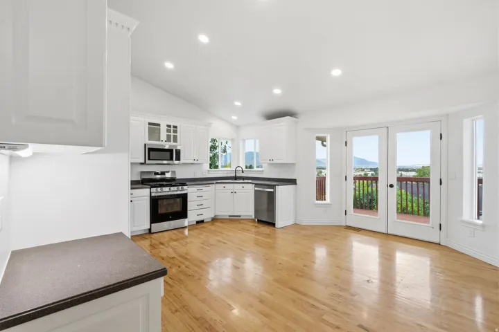 Vaulted ceiling with recessed lighting, light wood-finish flooring, white cabinetry, dark stone-finish countertops, and double glass doors leading to an outdoor deck