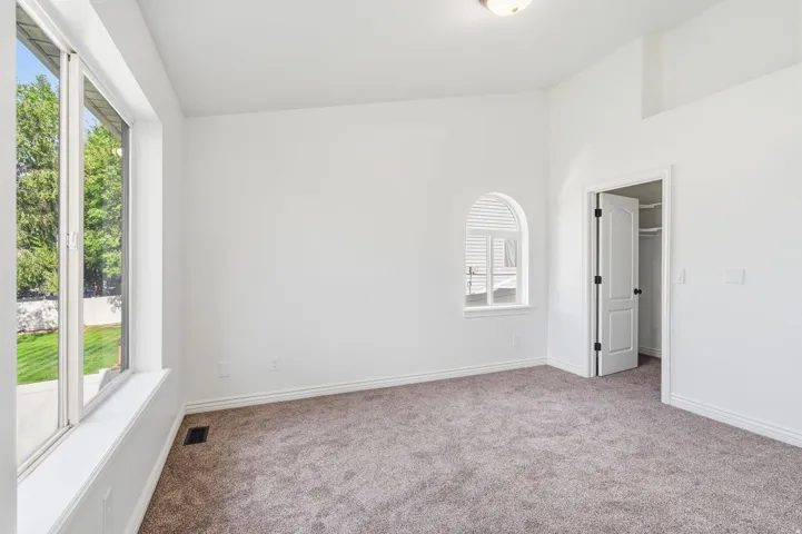 Spacious room featuring neutral carpeting, a large picture window, an arched window, and a white interior door