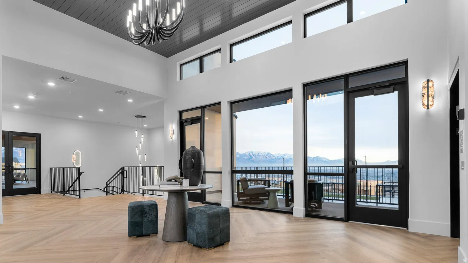 Two-story foyer featuring wood-finish flooring, a dark paneled ceiling, a modern chandelier, a built-in staircase with metal railings, and large windows with mountain scenery