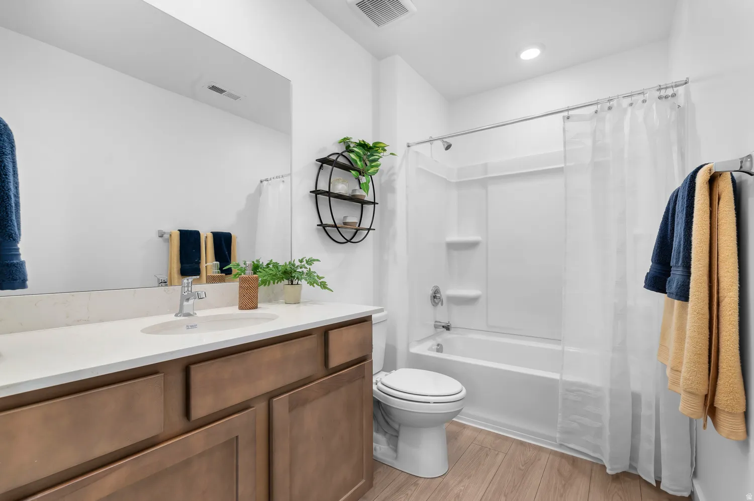 Wood-finish flooring, white vanity with integrated sink, rectangular mirror, full-size bathtub with shower, and recessed lighting