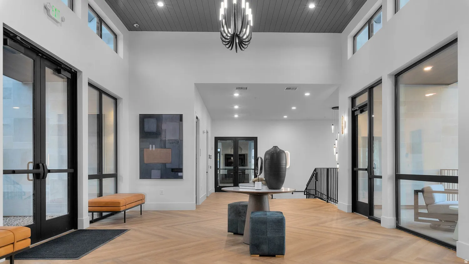 Vaulted ceilings with dark wood-paneled accents, herringbone wood-finish flooring, and black-framed glass entry doors