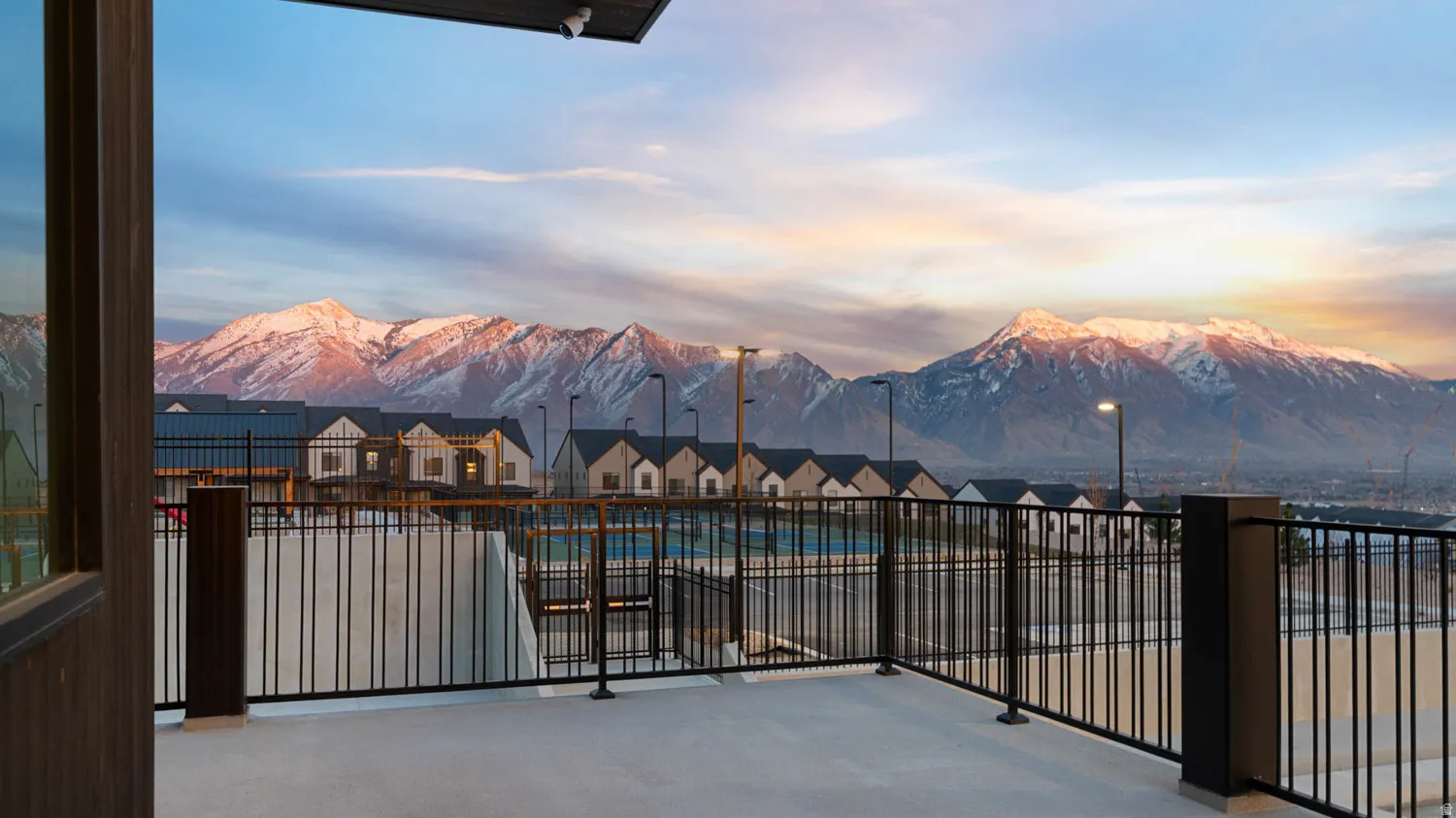 Expansive concrete balcony with black metal railings, overlooking a mountainous landscape and residential neighborhood