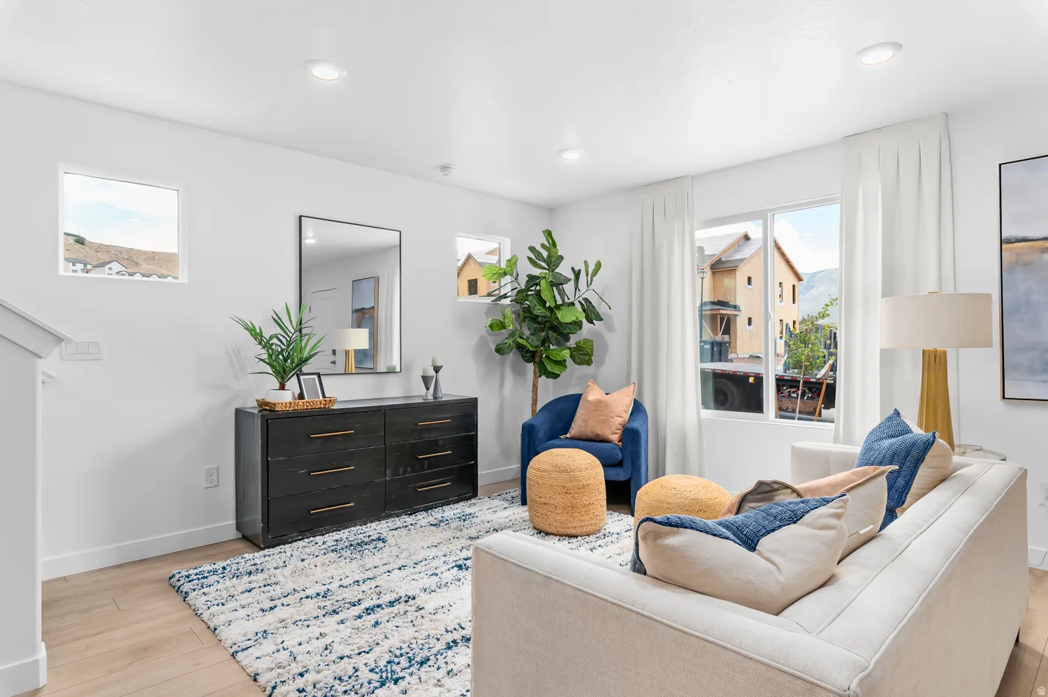 Recessed ceiling lighting, light wood-finish flooring, multiple windows, white wall finishes, and a dark wood-finish console with gold-tone hardware
