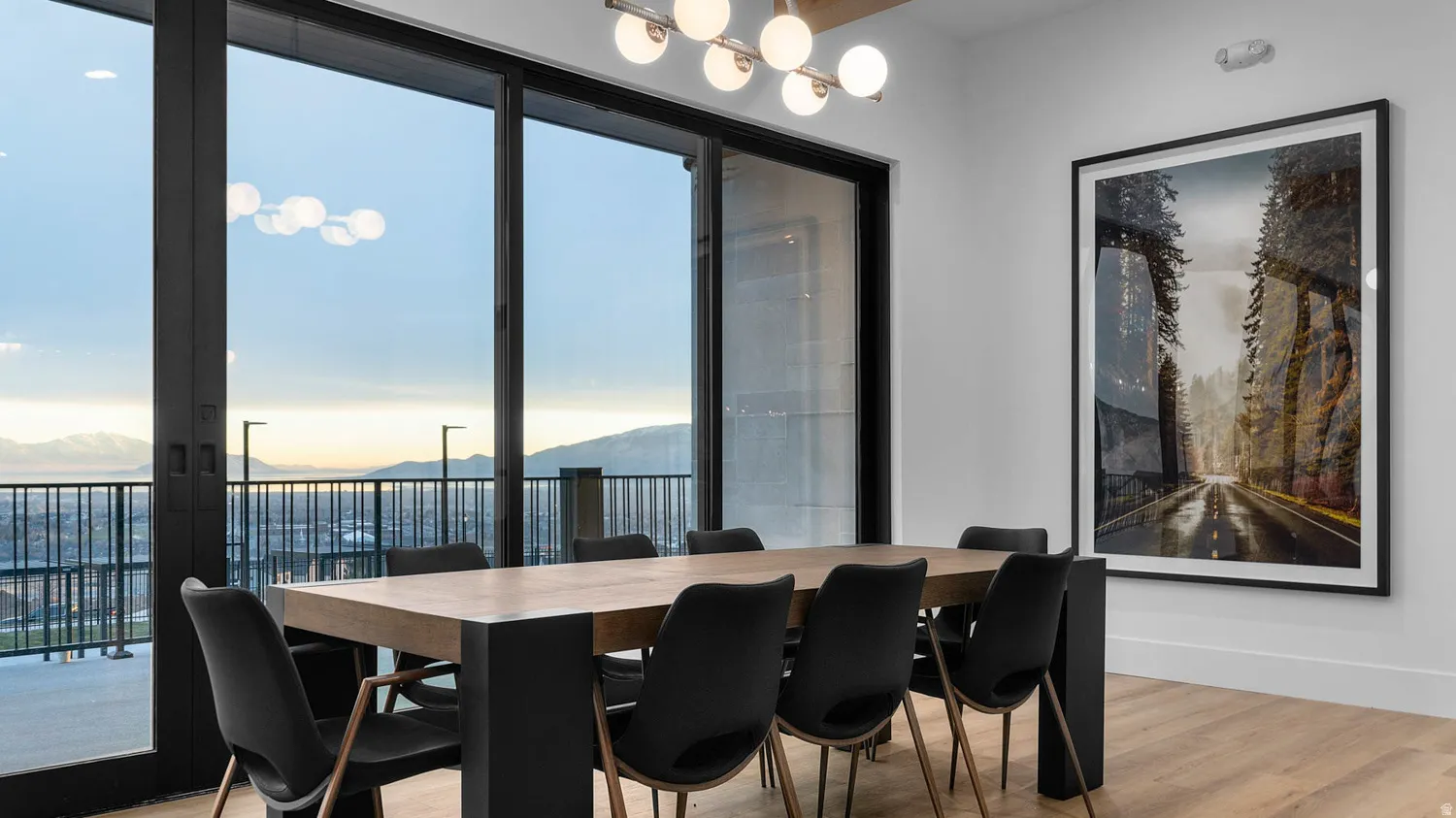 Expansive sliding glass doors, light wood-finish flooring, white walls, and a modern globe chandelier